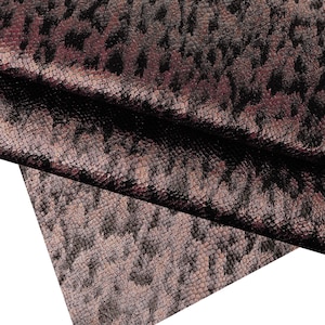 May include: Close-up of a textured fabric with a snakeskin pattern in shades of brown, black, and burgundy. The fabric is folded over, revealing the underside. The word "Marrone" is visible at the bottom.