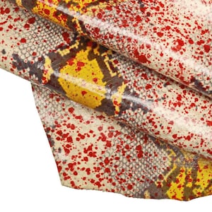 Peut inclure: Gros plan sur une peau de cuir texturée avec un motif peau de serpent. Le design présente une base d'écailles blanc cassé et grises, recouverte de taches jaunes et marron, et parsemée de taches de peinture rouge.
