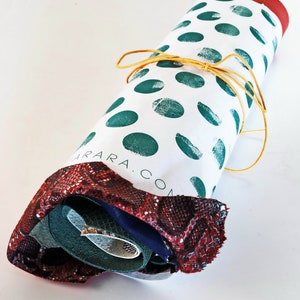 Peut inclure: Un &eacute;tui en tissu roul&eacute;, avec un fond blanc et des pois verts. Il est nou&eacute; avec une ficelle jaune. L'extr&eacute;mit&eacute; est rouge et pr&eacute;sente un motif peau de serpent. Le texte "ARARA.COM" est visible.