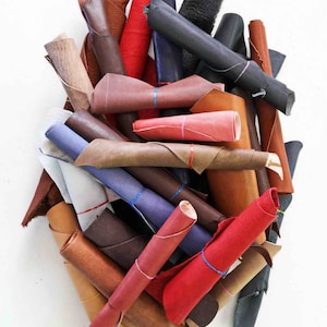 Pode incluir: Um monte de sobras de couro em v&aacute;rias cores, incluindo vermelho, marrom, bege e azul. O couro est&aacute; enrolado e amarrado com barbante.