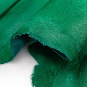 Può includere: Un pezzo di pelle bovina color verde smeraldo vibrante con una consistenza morbida a pelo corto sulla superficie superiore e una finitura scamosciata opaca e liscia sul lato inferiore. Il materiale è piegato per mostrare il contrasto.