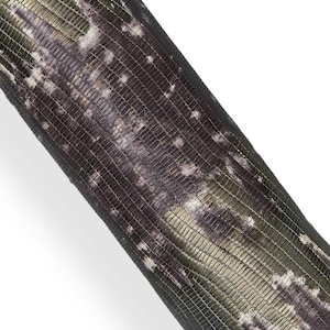 Puede incluir: Primer plano de un objeto cilíndrico texturizado con un patrón similar al de un reptil. La combinación de colores incluye tonos de verde, morado y blanco, creando un efecto de camuflaje. La superficie tiene una textura de rejilla.