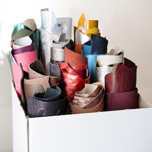 May include: A white box filled with rolls of colorful fabric scraps. The fabric scraps are in various colors, including red, blue, green, brown, and black.