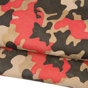 May include: Close-up of a fabric with a camouflage pattern. The design features irregular shapes in red, black, and tan colours. The fabric appears to be folded over, revealing the pattern's repetition.