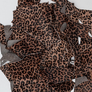 Könnte beinhalten: Haufen von Stoffresten mit Leopardenmuster. Die Stücke sind braun mit schwarzen Flecken, einige haben eine graue Rückseite. Die Reste sind auf einer weißen Oberfläche verstreut.