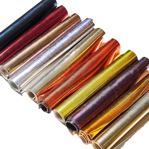 Peut inclure: Un assortiment de tissus métalliques enroulés dans différentes couleurs, notamment or, argent, rouge et bleu. Le tissu a une finition brillante et irisée.