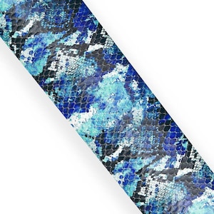 Puede incluir: Tira diagonal con un patrón de piel de serpiente en tonos azules, turquesas y negros. El diseño presenta un aspecto texturizado, similar a escamas, con un fondo blanco. El patrón recuerda a la piel de reptil.