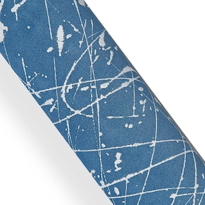 Può includere: Carta blu arrotolata con un design a spruzzi di vernice bianca. La carta ha una superficie strutturata ed è arrotolata, mostrando il motivo in una vista diagonale. La vernice bianca sembra essere applicata in un motivo casuale e astratto.