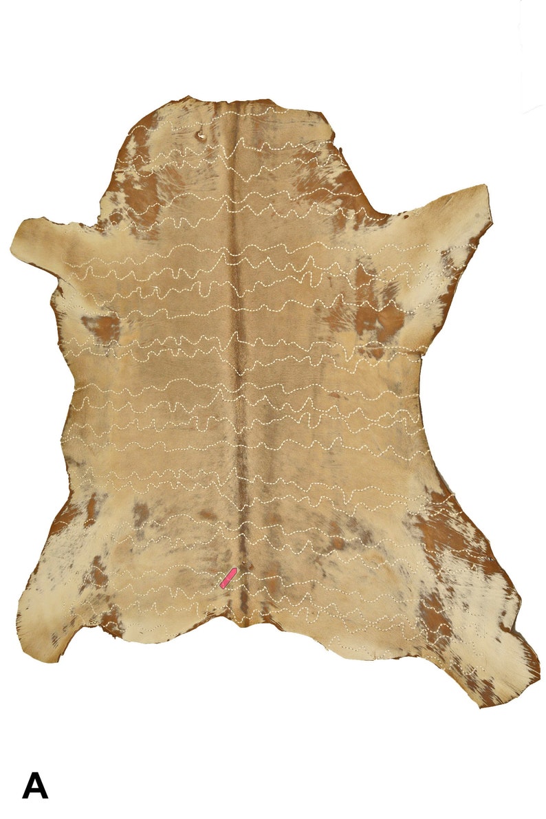 May include: A tan and brown cowhide rug with white stitching in a wavy pattern. The rug is approximately 3 feet by 4 feet.