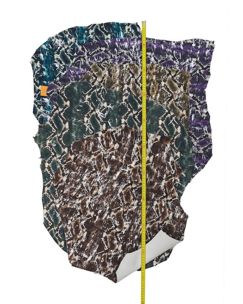 May include: A collection of multi-colored snakeskin leather hides. The hides are in shades of teal, purple, green, and brown. A yellow measuring tape is placed vertically along the hides, indicating the length of the leather.