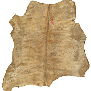 May include: A tan leather hide with a decorative stitching pattern. The stitching is done in a wavy line pattern.
