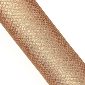 Könnte beinhalten: Eine Rolle Kunstleder mit Schlangenmuster. Das Material hat eine metallisch bronzefarbene Farbe mit einer strukturierten Oberfläche. Das Muster besteht aus kleinen, unregelmäßigen Formen.