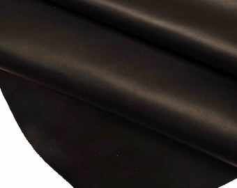 May include: Close-up of a sheet of dark brown leather. The leather has a smooth, slightly shiny surface with subtle variations in tone. The material is folded, revealing the texture and depth of the material.