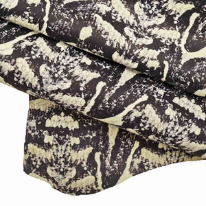 May include: Close-up of a fabric with a black and white snake skin pattern. The fabric is folded over itself, showing the texture of the material.