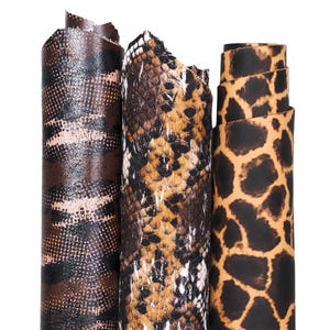 May include: Three rolls of patterned leather in shades of brown, tan, and black. The patterns include a snake skin design, a leopard print, and a geometric pattern. The rolls are tightly wound and stand upright against a white background.