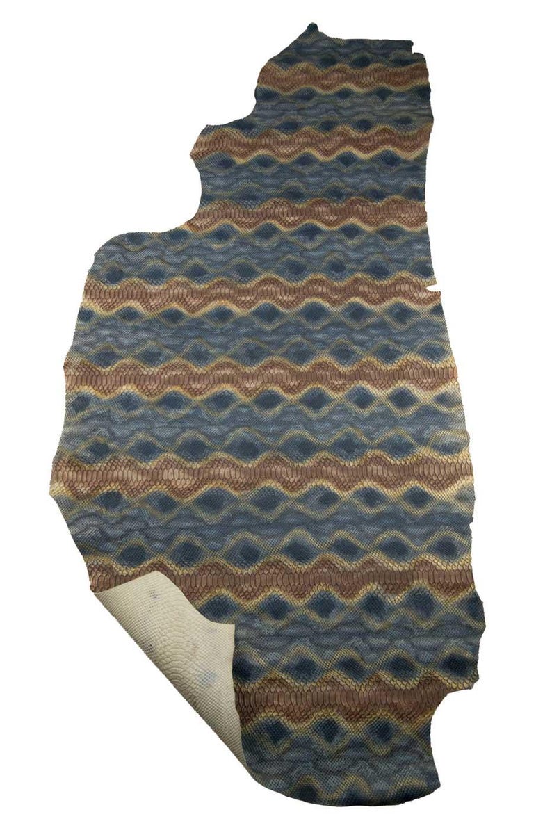 May include: A large piece of patterned leather with a blue, brown, and tan zigzag design. The leather has a textured surface and a light-colored underside. The edges are uneven, giving it a natural, organic shape.