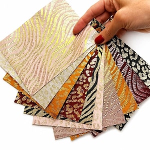 Op de afbeelding: Een verzameling rechthoekige stalen met diverse dierenprints in metallic goud, zwart, wit, bordeauxrood en oranje. De stalen hebben gestructureerde oppervlakken met zebrastrepen en luipaardvlekken, gerangschikt in een waaier.