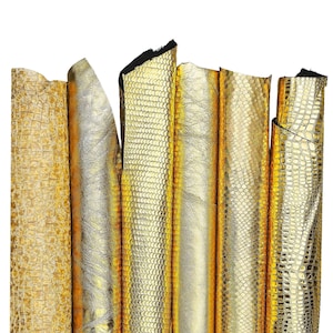 Puede incluir: Una colección de pieles de cuero doradas con diversas texturas, incluyendo patrones de cocodrilo y serpiente en relieve. Las pieles están dispuestas verticalmente, mostrando su brillo metálico y variaciones en el diseño de la superficie. Los bordes del cuero son visibles.