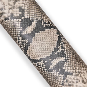 Könnte beinhalten: Nahaufnahme eines gerollten Materials mit Schlangenmuster. Das Muster weist eine Mischung aus beigen, grauen und schwarzen Schuppen auf, wodurch ein strukturiertes Aussehen entsteht. Das Material ist gebogen, was darauf hindeutet, dass es sich um eine Hülle oder ein dekoratives Element handeln könnte.
