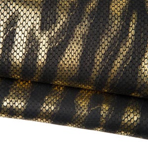 May include: Close-up of a textured fabric with a black and gold snakeskin pattern. The material has a scaly texture with gold accents, creating a shimmering effect. The fabric is folded over, revealing the underside.