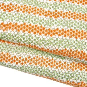 Puede incluir: Primer plano de una tela con un patrón repetitivo de puntos naranjas y verdes sobre un fondo blanco. Los puntos están dispuestos en filas horizontales, creando una apariencia texturizada. La tela está doblada, mostrando la continuidad del patrón.