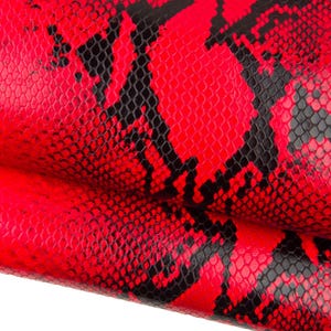 Op de afbeelding: Close-up van een levendig rood leermateriaal met een zwart slangenpatroon. De textuur is gedetailleerd en toont de schubben en natuurlijke plooien van het materiaal. De kleur is een helder, felrood.