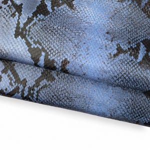 Könnte beinhalten: Nahaufnahme von blauem und schwarzem Schlangenleder. Das Leder hat ein strukturiertes, schuppiges Muster mit einem Farbverlauf aus hellen und dunklen Blautönen. Das Schlangenleder ist gefaltet und zeigt die Unterseite.