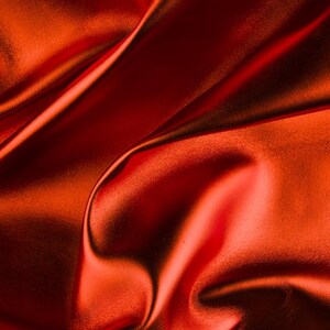 May include: Close-up of a smooth, red fabric with soft folds and wrinkles. The fabric has a subtle sheen and a luxurious feel.