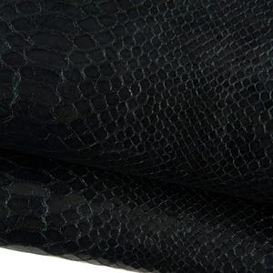 May include: Close-up of black leather with a textured, reptile-like pattern. The material appears to be folded, revealing the underside. The surface has a subtle sheen, suggesting a high-quality finish. This leather is suitable for various crafting projects.