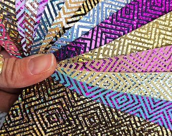 May include: A hand holds a fan of colorful, patterned papers. The papers display a geometric diamond design in various colors, including gold, purple, blue, and silver. The papers have a shiny, metallic finish, reflecting light.