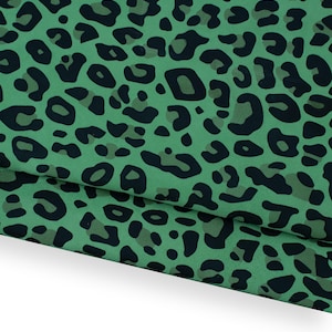 Peut inclure: Tissu vert avec un motif léopard noir. Le tissu est plié, révélant les taches répétées. Le mot "Verde" est imprimé en bas de l'image.