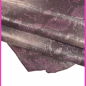 Könnte beinhalten: Nahaufnahme eines strukturierten Ledermaterials mit Schlangenmuster. Das Leder weist Farbtöne von Lila, Grau und Gold auf, wodurch ein schimmernder Effekt entsteht. Das Material ist gefaltet und zeigt seine Textur und Farbvariationen.