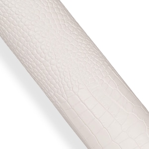 Könnte beinhalten: Eine Rolle weißen Kunstledermaterials mit einem strukturierten Krokodil- oder Alligatorhautmuster. Das Material ist diagonal aufgerollt und zeigt die detaillierte Oberflächenstruktur und Farbe.