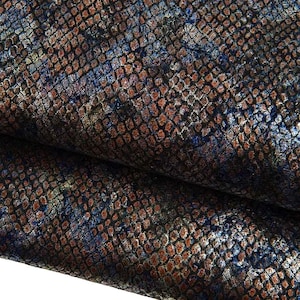 May include: A textured material featuring a repeating snakeskin pattern in shades of copper, brown, and deep blue. The surface displays a metallic sheen with a fine, grid-like overlay that creates a multi-dimensional appearance across the folded fabric.