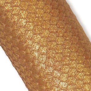Può includere: Un foglio di materiale testurizzato caratterizzato da un motivo ripetitivo a scaglie color oro metallizzato. La superficie presenta una finitura granulosa e scintillante con un design coerente a scaglie di pesce intrecciate.