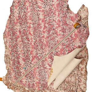 Peut inclure: Une grande pi&egrave;ce de cuir de peau de serpent avec un motif de peau de serpent rouge et marron. Un m&egrave;tre ruban et une &eacute;tiquette sont visibles sur le cuir. Le dessous du cuir est de couleur beige clair.