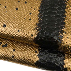 May include: Close-up of a textured material with a gold and black snakeskin pattern. The gold section has small black spots. A thick black stripe runs vertically through the center of the image.