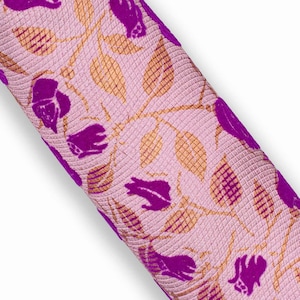 Può includere: Tessuto arrotolato con sfondo rosa e motivo ripetuto di fiori viola e foglie dorate. Il tessuto ha un aspetto strutturato e trapuntato. La parola "Rosa" è stampata in basso a sinistra.