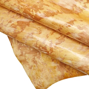 May include: A close-up of a piece of yellow leather with a brown and white pattern. The leather is folded in half and the edges are visible.