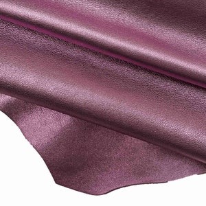 Peut inclure: Gros plan sur un morceau de cuir souple, texturé, violet avec un reflet métallique. Le cuir est plié sur lui-même, créant un drapé doux et fluide.