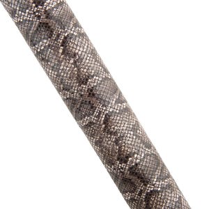 May include: Close-up of a cylindrical object with a snakeskin pattern. The pattern features a mix of grey, black, and white scales. The object is angled diagonally against a white background.