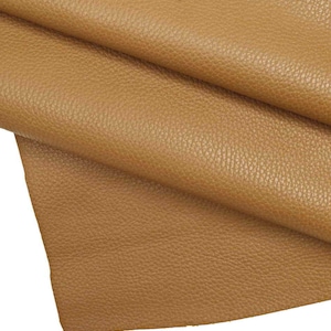 May include: A close-up of a piece of brown leather with a textured surface. The leather is folded in half, showing the inside of the fold.