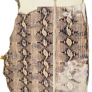 Op de afbeelding: Een stuk slangenleer met een bruin en zwart patroon. Het leer wordt gemeten met een meetlint, dat een lengte van 114 cm laat zien.