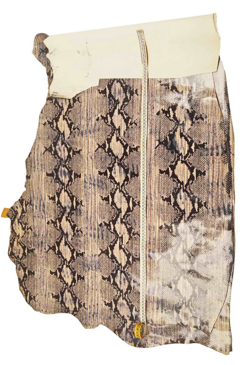 Op de afbeelding: Een stuk slangenleer met een bruin en zwart patroon. Het leer wordt gemeten met een meetlint, dat een lengte van 114 cm laat zien.