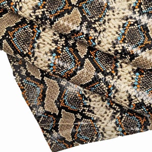 Pode incluir: Close-up de um tecido de pele de cobra com um padr&atilde;o preto, marrom, laranja e azul.