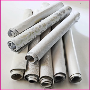May include: A collection of rolled white leather hides with various textures and patterns. Some rolls have embossed reptile scales, while others feature floral or geometric designs. The leather appears to be of high quality, with a smooth or textured finish.