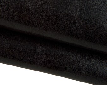 May include: Close-up of black leather with a textured surface. The leather is folded over, revealing the grain and subtle colour variations. The material appears soft and supple, suitable for various crafting projects.
