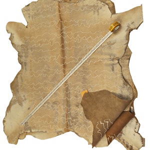 May include: A large piece of tan leather with a white stitching pattern. A yellow measuring tape is lying on top of the leather.