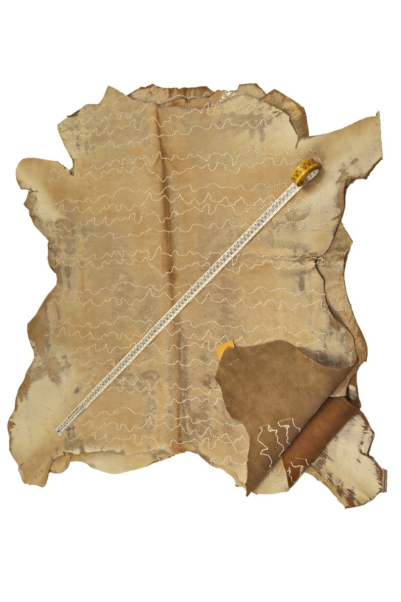 May include: A large piece of tan leather with a white stitching pattern. A yellow measuring tape is lying on top of the leather.