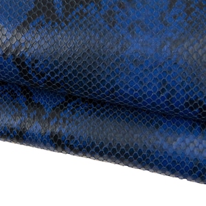 Puede incluir: Primer plano de un patrón de piel de serpiente texturizado azul y negro. El patrón presenta un diseño similar a una escama con diferentes tonos de azul y negro, creando una apariencia realista de piel de reptil. El material parece ser cuero.